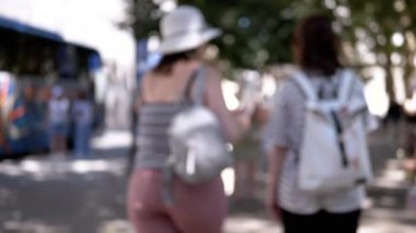 Sırt çantalı iki kadın güneşli bir günde şehir caddesinde yürürler. Anonim ve atmosferik bir his için bulanıklaşırlar. Seyahat, turizm ve şehir hayatı projeleri için ideal.