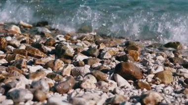 Güneşli bir kumsalda çakıl taşlarının üzerinde süzülen yumuşak deniz mavisi dalgaları sakinleştirici ve sakin bir atmosfer yaratır. Seyahat, doğa ya da spa videoları için mükemmel.