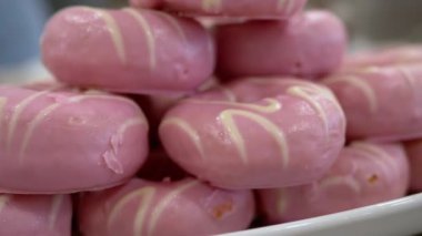 Bir tabak pembe çörek, beyaz çizgili, tatlı gösterisinin bir parçası. Yumuşak odaklanma şenlikli bir olay olduğunu gösteriyor. Baştan çıkarıcı ve lezzetli..