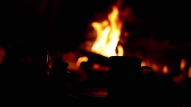 Kamp ateşinin yanında bir kupa ve kavanozla bir hayat sahnesi. Ateşin sıcaklığı rahat bir atmosfer yaratıyor. Kamp ve açık hava teması için mükemmel..