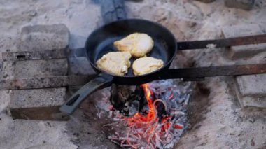 Tavuk göğüsleri çatırdayan bir kamp ateşinin üstünde çatırdayan demir bir tavada cızırdıyor. Kamp yapmak ya da açık hava maceraları için mükemmel sıcak ve davetkar bir ortam yaratıyor. Pişirilmiş etin kokusu havayı dolduruyor.