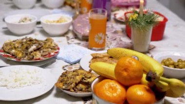 Geleneksel yemekler ve renkli meyvelerle dolu güzel bir masa, Yeni Yıl arifesi kutlaması için sıcak ve davetkar bir ortam yaratır. Titrek mum sihre bir dokunuş ekler