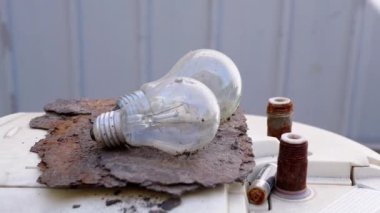 Paslı bir metal yüzeyde duran iki ampulün yakın çekim görüntüsü. Hurda metal ve tuğla ipuçlarının bulanık arka planı bir hurdalık ayarında.