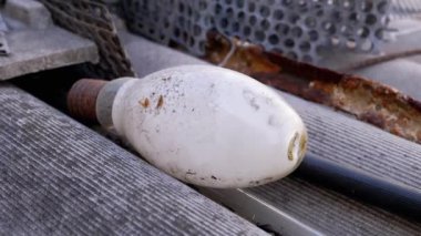 Paslı metal bir yüzeye yayılmış iki tozlu, gözden çıkarılmış parlak ampul, eskimişlik ve atıkları gösteriyor. Bu yakın çekim ampulleri, iplikleri ve çevresindeki toprağı vurguluyor.