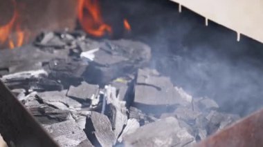 Izgarada yanan kömürlere yakın çekim, alevler dumanın arasında yanıp sönüyor, canlı ve dinamik bir sahne yaratıyor, yemek programları ve barbekü ile ilgili görseller için mükemmel..