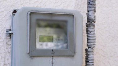 Duvardaki eski ve tozlu bir elektrik sayacının yakın çekim görüntüsü. Ekrandaki numaralar odak dışı. Enerji tüketimini, faturaları veya modası geçmiş teknolojiyi temsil eder.