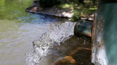 Temiz su paslı bir borudan yavaş çekimde bir gölete akar. Su kıtlığı ve kirlilik sorunları.