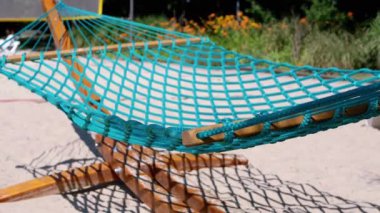 Turkuaz halat hamağı güneşli bir sahilde hafif bir esintide sallanıyor. Seyahat, eğlence ve tatil temaları için mükemmel..