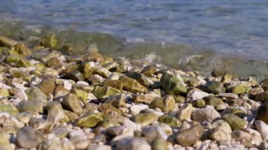 Güneşli bir günde çakıl taşlı bir plajda süzülen yumuşak dalgaların yakın çekimi. Pürüzsüz, renkli taşlar rahatlatıcı ve meditasyon sahnesi yaratır. Doğa, seyahat ve rahatlama ile ilgili projeler için mükemmel..