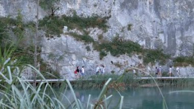 Turistler, sazlıklarla çevrili bir kaya duvarının yanındaki tahta köprü boyunca yürürler. Gölün berrak suyu doğanın huzurunu yansıtır. Sakin atmosfer çarpıcı keşfi davet ediyor.