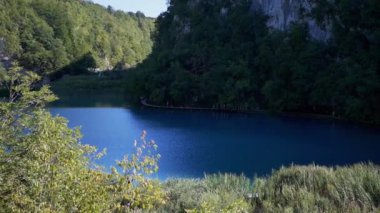 Turistler Plitvice Gölleri Ulusal Parkı 'ndaki bir gölün kıyısındaki ahşap bir patika boyunca yürüyorlar. Turizm ve çevre sorunları kavramı
