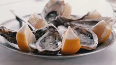 Buz ve limon dilimli metal bir tabakta iki bardak soğuk beyaz şarapla servis edilen taze açılmış istiridyeler. Lüks bir deniz ürünleri deneyimi..