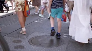 Yaya geçidi üzerinden şehir caddesini geçen yayalar. Yaz günü, bacakların ve ayakların düşük açılı görüntüsü, çeşitli kalabalık, kentsel çevre.