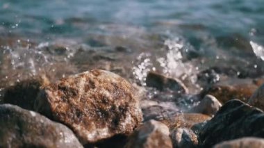 Yumuşak dalgalar güneşli bir sahilde pürüzsüz taşları okşar, sakin ve sakin bir atmosfer yaratır. Seyahat, doğa ve rahatlama projeleri için mükemmel..