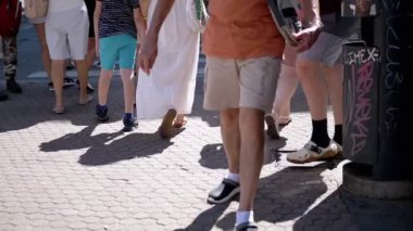 Asfalt bir cadde boyunca yürüyen kalabalığın bacakları ve ayakları. Düşük açılı çekim şehir yaşamının hareketini ve ritmini yakalar..