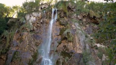 Görkemli bir şelale, yemyeşil ormanlarla çevrili kayalık bir uçurum yamacından aşağı dökülüyor. Bu nefes kesici doğa harikası huşu ve sükunete ilham verir..