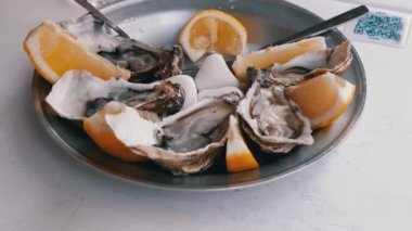 Limon dilimli metal bir tabakta servis edilen taze istiridyelerin yakın çekimi, tadını çıkarmaya hazır. Deniz ürünleri, restoran ve lüks yaşam tarzı temaları için mükemmel..