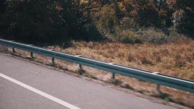 Pürüzsüz asfalt bir yol, korkuluklar ve renkli yaprakların yer aldığı sonbahar manzarası. Seyahat, doğa ve ulaşım projeleri için ideal.