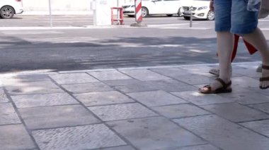 Güneşli bir günde bir kadın ve bir çocuk kaldırımda sandalet giyerek yürür. Arabalar arka planda yolda gidiyor. Bu görüntüler aile, seyahat ve yaz tatili kavramını temsil ediyor..