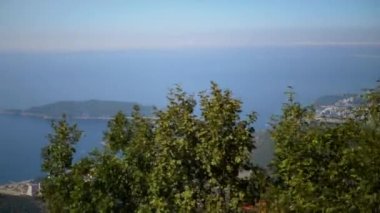 Karadağ 'ın görkemli kıyıları, deniz, tekne ve Sveti Stefan adasına bir göz atarak yemyeşil yaprakların arasından görülüyor. Doğa ve seyahat videoları için ideal.