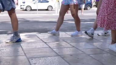Bir yaz gününde yürüyen ayaklar. Çeşitli ayakkabılar giyen insanlar şehir kaldırımında yürüyorlar. Bu yavaş çekim, yaşam tarzı projeleri için ideal dinamik bir enerji getiriyor..