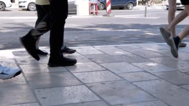 Güneşli bir yaz gününde yürüyen çeşitli ayakların yakın çekimi. Bu büyüleyici yavaş çekim, insanlar yürürken şehir hayatının özünü yakalar. Seyahat, yaşam tarzı veya şehir temalı projeler için mükemmel.
