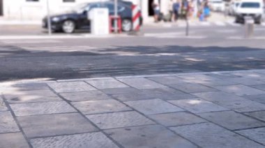 Güneşli bir günde, arka planda bulanık arabaların ve yayaların olduğu boş bir kaldırım ve yaya geçidi. Şehir hayatı, yaya güvenliği veya bekleme projeleri için mükemmel..
