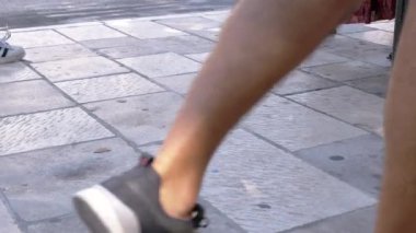 Kapalı bir kaldırımda yürüyen ayaklar, şehir ortamındaki hareketleri ve çeşitli ayakkabıları yakalıyor..