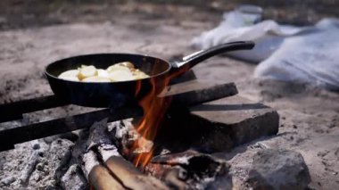 Kamp ateşi üzerinde tavada cızırdayan patatesler. Köy yemekleri ve titreyen alevler rahat bir atmosfer yaratıyor..