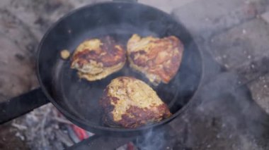 Kamp ateşinin üstünde üç parça tavuk kızartması, duman yükseliyor, kırsal alanda yemek pişirme sahnesi yaratıyor. Kamp, yemek, yemek ve açık havada yaşama ile ilgili projeler için ideal.