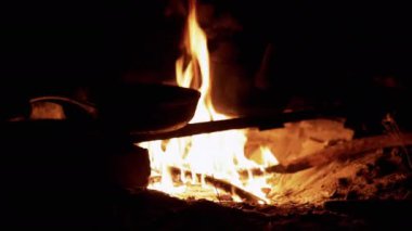 Bir tava çatırdayan bir kamp ateşinin üzerinde oturur ve gece gökyüzünün altında yemek pişirmeye hazırdır. Alevlerin sıcaklığı rahat bir atmosfer yaratıyor..