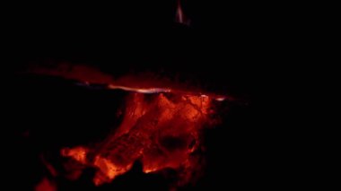 Yukarıda yanan bir kütükle karanlıkta parlayan için için için yanan közlerin yakın çekimi sıcak ve büyüleyici bir manzara yaratır. Yangın, sıcaklık, kamp veya doğa ile ilgili projeler için mükemmel..