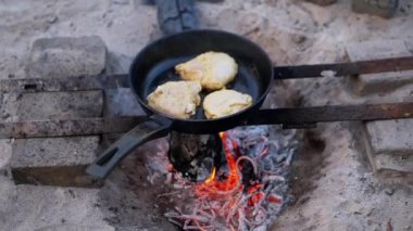Açık ateşte tavuk pişirmenin basitliğini hisset. Dökme demir bir tava, parlayan közlerin arasına yerleştirilmiş, kırsal metal bir standın üzerinde oturur ve açık hava yemeklerine otantik bir dokunuş ekler. Tam oldu.