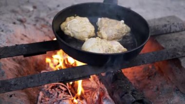 Üç tavuk budu açık bir kamp ateşinde tavada kızarıyor, kırsal bir açık hava yemek sahnesi. Bu video kamp ateşi mutfağının sıcaklığını ve basitliğini anımsatıyor. Seyahat ve yemek programları için mükemmel..