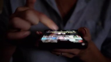 Düşük ışıkta akıllı telefon ekranında gezinmek için parmağını kullanan bir kişi, gece geç saatlerde tarama ya da içerik tüketimi öneriyor. Teknoloji ve modern yaşam hakkındaki projeler için ideal.