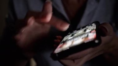 Karanlık bir odada sosyal medyada gezinen ellerin yakın çekimi, kullanıcıların parmaklarını aydınlatan telefonun ışığı.