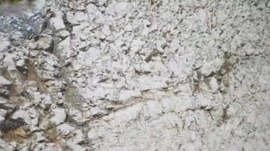 Hareket halindeki bir araçtan görülen seyrek bitki örtüsüyle kayalık bir dağ yamacının yakın görüntüsü. Kayaların sert dokusu ve doğanın esnekliği vurgulanmıştır. Potansiyel hakkında farkındalığı artırır