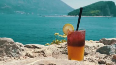 İki tonluk canlı bir kokteyl büyüleyici bir okyanus manzaralı kayalık bir sahilde oturur. Mükemmel yaz içeceği..