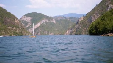 Arnavutluk 'ta bir rezervuar olan Koman Gölü' nün manzarasında, dağlarla çevrili bir kayanın üzerinde bir haç duruyor. Huzurlu manzara, inancı ve huzuru yansıtıyor..