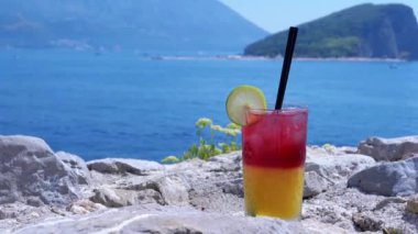 Huzurlu bir körfeze bakan kayalara iki tonluk kokteyl serinletici, mükemmel bir sahil tatilinin özünü somutlaştırıyor..