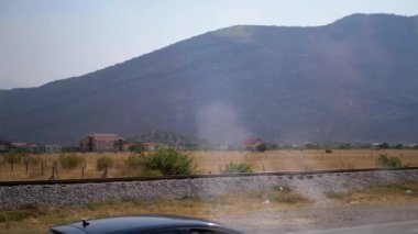 Huzurlu bir dağ manzarası yol kenarından, demiryolu rayları ön planda, evler ortada ve büyük bir dağ arka planda, huzurlu bir seyahat sahnesi oluşturarak gözler önüne seriliyor..