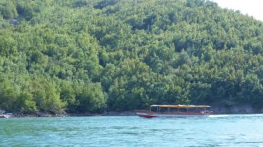 Bereketli yeşil tepelerle çevrili, pitoresk bir nehir boyunca seyreden turist teknesinin manzarası. Seyahat, turizm ve doğa projeleri için mükemmel. Nehrin dinginliğini ve güzelliğini sergiliyor.