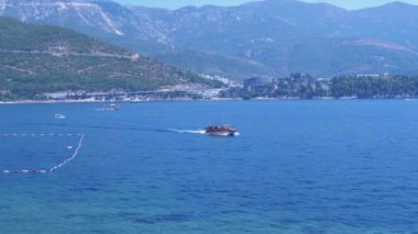 Turuncu turizm teknesi Karadağ 'ın Adriyatik kıyısı boyunca yol alıyor. Budva Riviera 'nın güzel manzarası, dağlar ve oteller. Yaz güneşli bir gün, açık bir gökyüzü, mavi bir su. Seyahat için mükemmel bir arkaplan