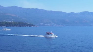 Karadağ 'ın Budva kenti yakınlarındaki Adriyatik Denizi' nde yol alan bir turizm teknesi, çarpıcı sahil şeridi, dağlar ve geçen bir yatı gösteriyor..