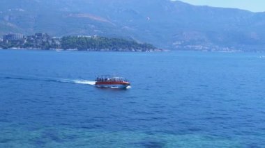 Sveti Nikola Adası yakınlarındaki Adriyatik Denizi 'nde seyreden bir turist botu, Karadağ kıyı şeridi manzarası ve yemyeşil dağlar sunuyor. Seyahat ve turizm projeleri için mükemmel bir zemin.