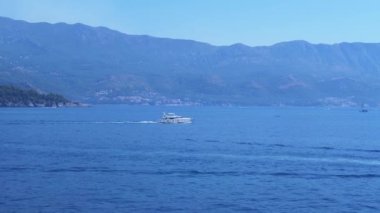 Karadağ 'ın Budva kenti yakınlarındaki sakin Adriyatik Denizi' nde, arkasında dağlar ve bir kasaba bulunan beyaz bir yat seyrediyor. Lüks, seyahat ve huzur dolu bir güzellik manzarası..