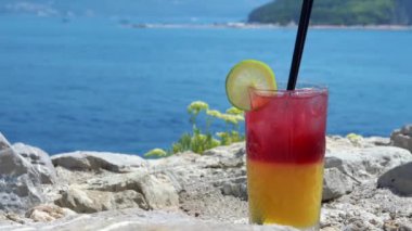 Taş bir duvarda renkli limonlu kokteyl var. Resmedilmeye değer bir ada koyuna bakıyor. Seyahat ve eğlence temaları için mükemmel.