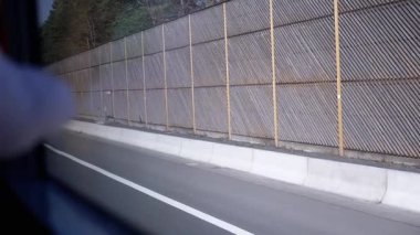 Hareket halindeki bir aracın yol kenarında gürültü bariyeri olan bir otobandaki acil durak bölgesinden geçerken görüntüsü. Seyahat, güvenlik ve altyapı videoları için iyi.