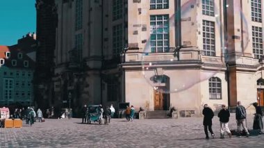 Dresden, Almanya - 11 Nisan 2025: Dev sabun köpükleri Dresden meydanında yüzüyor, tarihi binaları ve Martin Luther anıtını geçiyor. Seyahat ve şehir hayatı videoları için mükemmel..