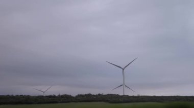 Rüzgar türbinleri bulutlu gri gökyüzüne karşı dimdik ayakta durarak temiz enerji üretir. Çevre, enerji ve teknoloji projeleri için ideal.